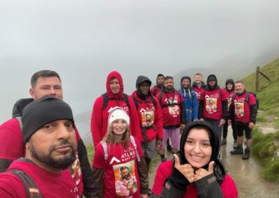 a group of people wearing pink fundraising jumpers standing in the rain with mount snowden in the background from seven hair and body one person is holding their thumbs up at the camera