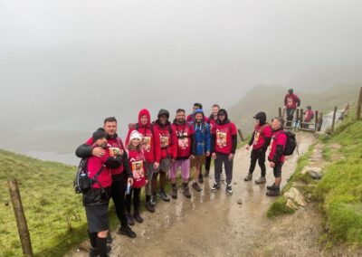 a group of people wearing pink fundraising jumpers standing in the rain with mount snowden in the background from seven hair and body