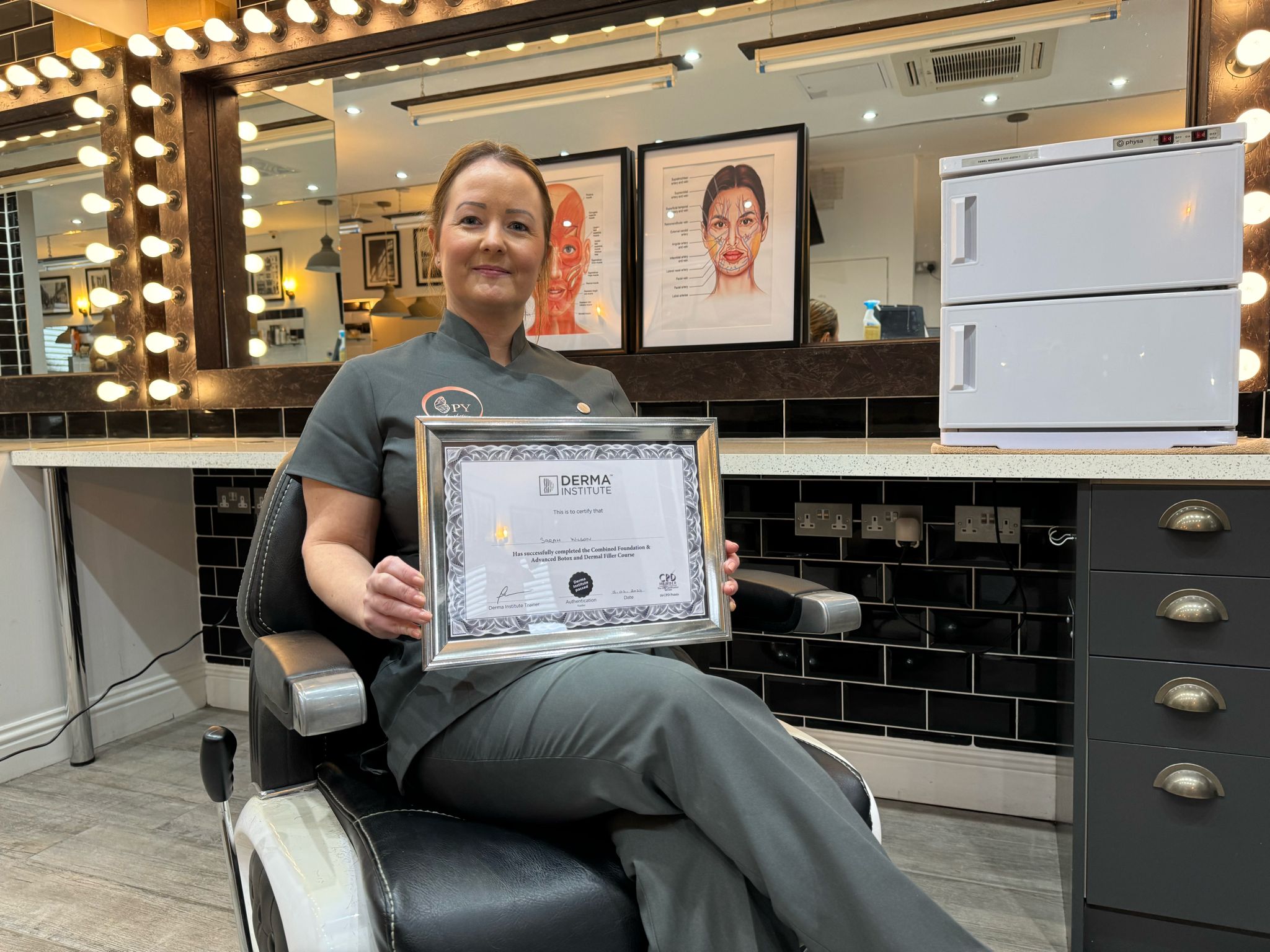 Image of woman sat in a chair holding an aesthetic prescriber certificate