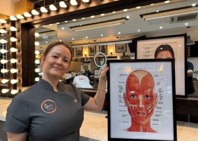 Lady holding a framed medical image of the muscles of the face smiling at the camera in seven hair and body barbers in peterborough
